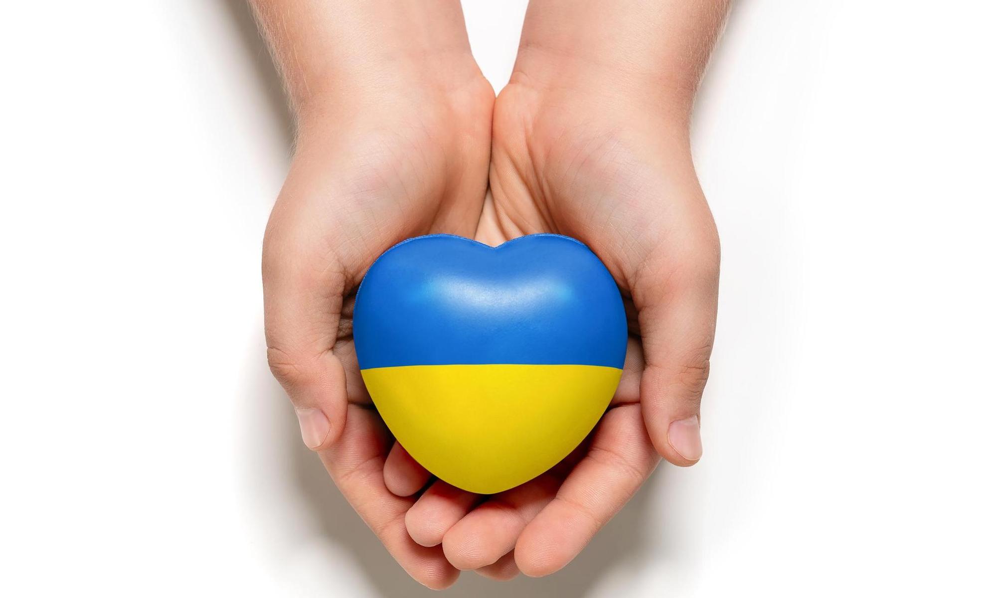 händer som håller i ett hjärta med Ukrainas flaggas färger